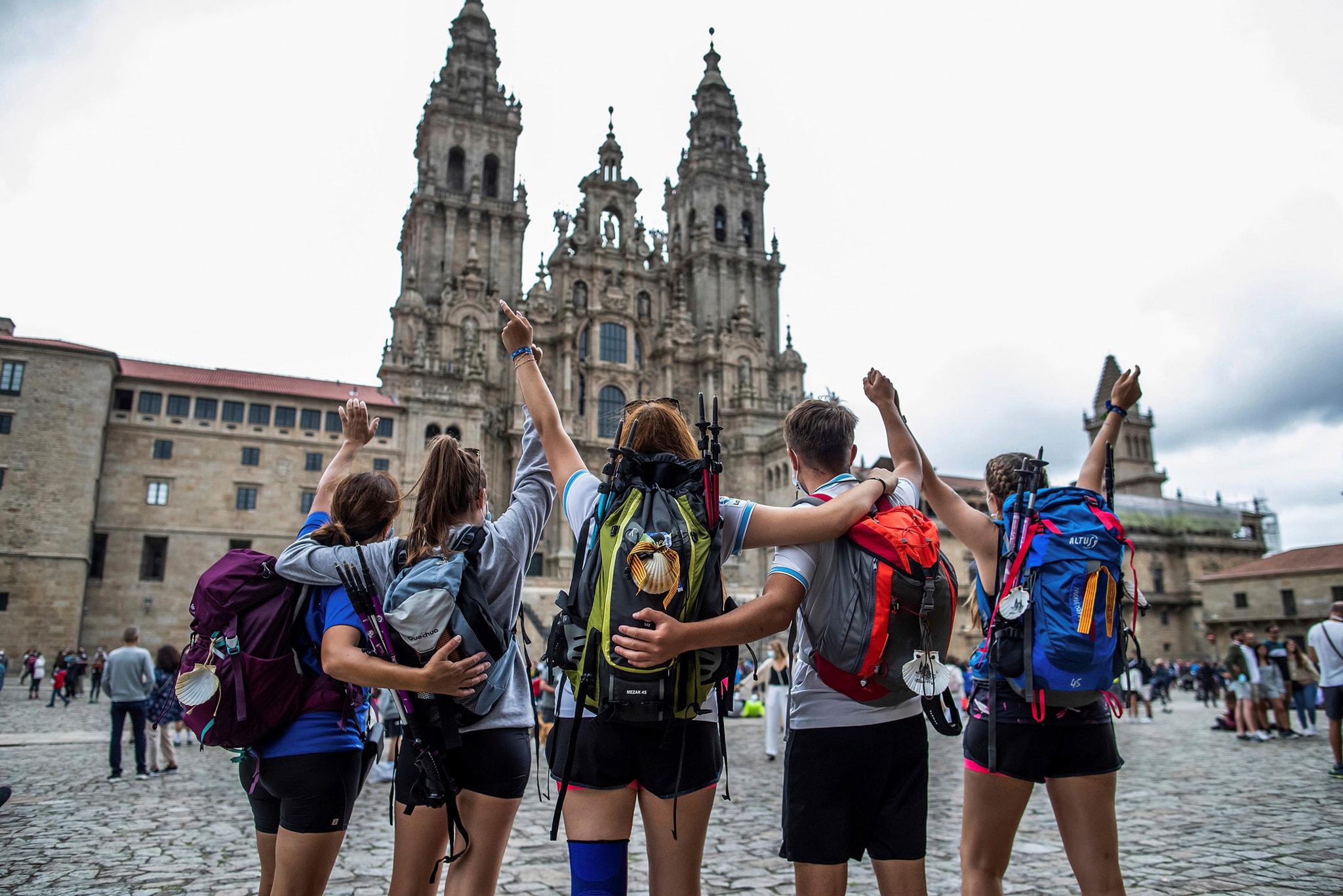 Grupo de peregrinos celebrando su llegada a la Catedral de Santiago de Compostela con los brazos en alto y expresiones de alegría